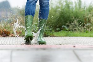 women in green rain boots splashing in puddle