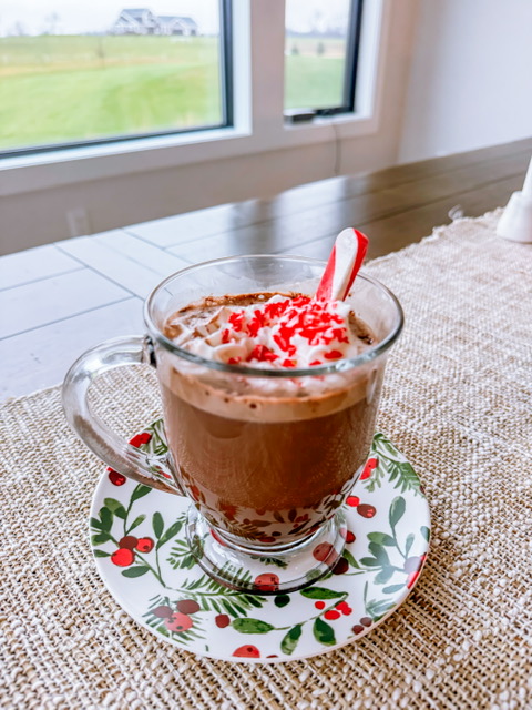 hot chocolate in glass mug with whipped cream and crushed candy canes on top